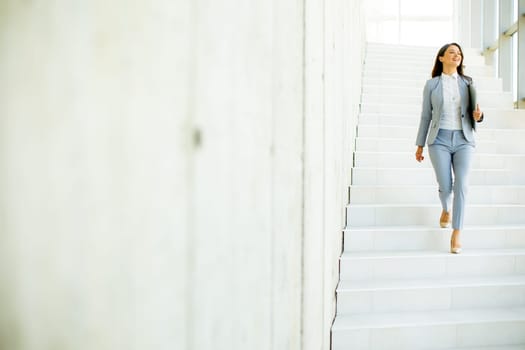 Young business woman walking down the stairs and holding laptop at the office hallway