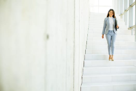 Young business woman walking down the stairs and holding laptop at the office hallway