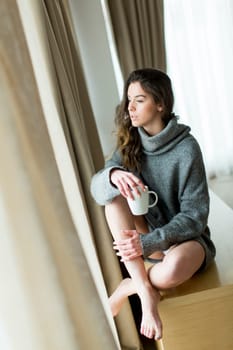 Pretty young woman with cup of coffee by the window