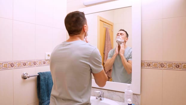 Man lathering shaving foam on his face, preparing for a shave in a modern bathroom