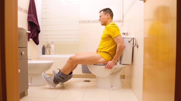 Man experiencing abdominal pain while sitting on the toilet in a bathroom