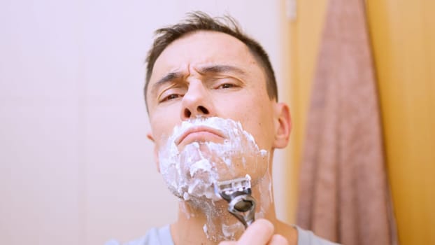 Caucasian man shaving his beard with a razor and shaving cream in the bathroom