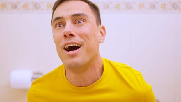 Caucasian man wearing yellow t shirt feeling relieved after using toilet in bathroom
