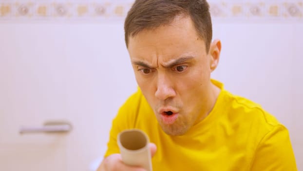 Man sitting on toilet discovers there is no toilet paper left on the roll and makes a surprised face