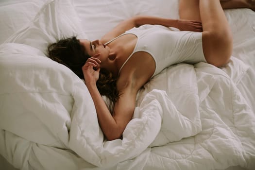 Attracttive young woman lies in white bed