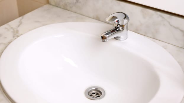 Clean white bathroom sink with chrome faucet on marble countertop