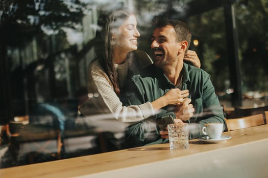 Young couple shares tender moments at a café, surrounded by greenery and natural light, as they connect over warm drinks and playful gestures