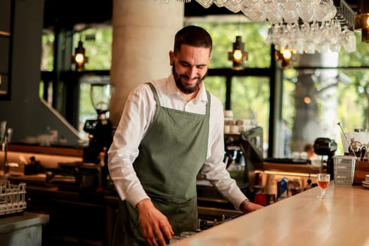 With a warm smile, the bartender skillfully crafts cocktails in a lively bar, where sunlight floods through large windows, creating a vibrant atmosphere
