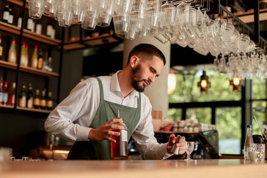 In a lively bar setting, a confident bartender mixes a fresh cocktail, showcasing his expertise with a bottle in hand, ready for the night's rush