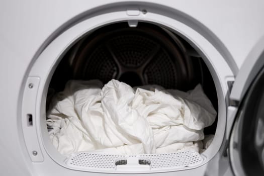 White bedsheets in modern tumble dryer close up laundry scene.