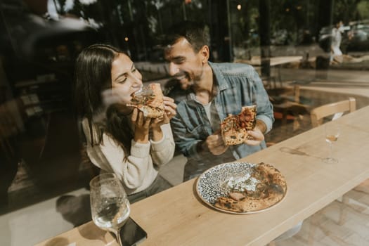 A couple delightfully indulges in slices of pizza at a charming café, surrounded by bright, airy ambiance and good vibes, savoring each bite together