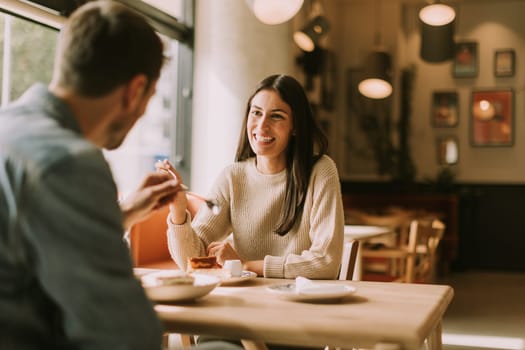 A couple enjoys a delightful moment in a warm café, sharing laughter and delicious treats while basking in the cozy ambiance filled with natural light.