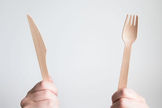 Hands holding wooden cutlery set against white background.