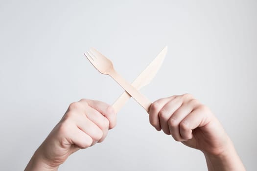 Hands holding wooden cutlery against white background.