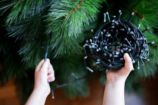 Child preparing Christmas tree with string lights.