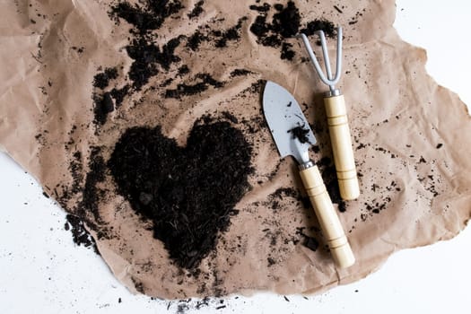 Gardening tools with heart shaped soil on brown paper for creative landscaping.