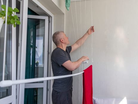 Man hangs the clothes on the roller dryer on the balcony