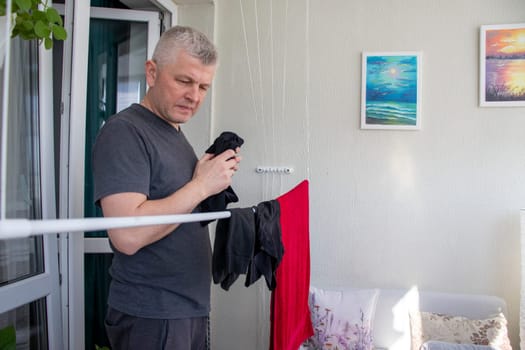 Man hangs the clothes on the roller dryer on the balcony.