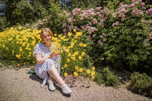 A woman is sitting in a field of yellow flowers. She is holding a glass of wine and smiling