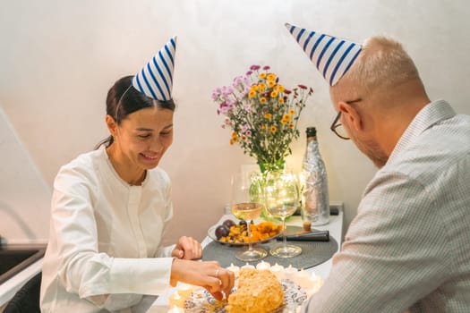 Here's a caption under 150 characters describing the image: A man and woman, wearing party hats, celebrate with food and drinks at an intimate table setting.