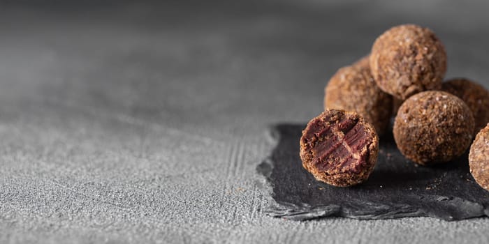 Decorating of artisan chocolate truffle candies with berry and fruit filling on dark background from confectionary. Handmade or handcrafted bonbons, chocolatier concept. Horizontal banner, copy space