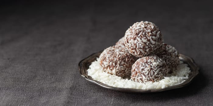 Artisan chocolate coconut truffle candies on dark background from confectionary. Handmade or handcrafted bonbons, chocolatier concept. Horizontal banner, copy space