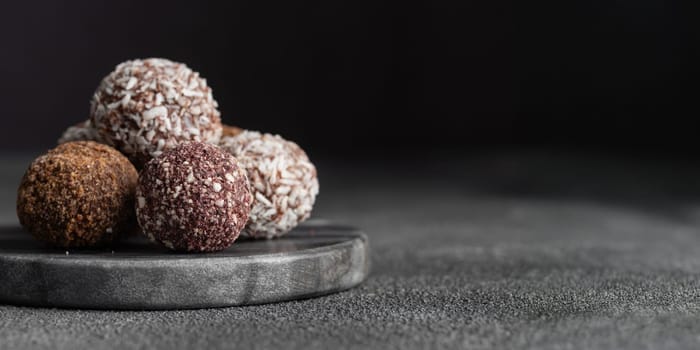 Assortment of gourmet handcrafted vegan chocolate truffle candies on dark marble background from premium confectionary. Handmade bonbons chocolatier concept. Horizontal banner with copy space