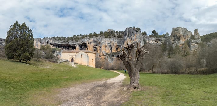 A quaint hermitage set against striking cliffs and a peaceful green landscape, evoking history and tranquility.