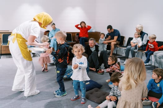 Actress with a bowl distributes treats to children and parents in a kindergarten. High quality photo