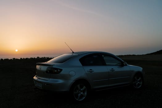 Silver car stands on the seashore against the backdrop of a colorful sunset. High quality photo