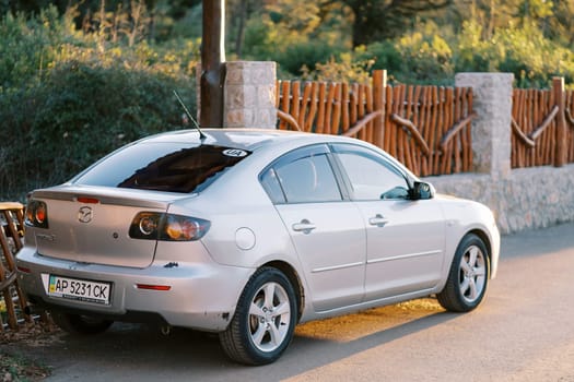 Silver Mazda stands near a wooden fence on the road. Side view. High quality photo