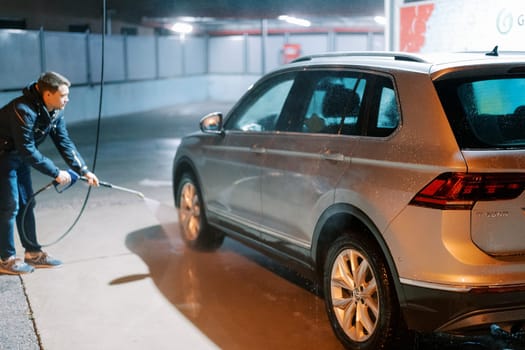 Young man washing a car with a hose at a self-service car wash. High quality photo