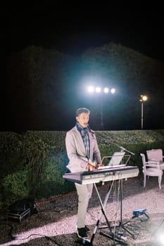 Band vocalist plays the synthesizer and sings in the night garden under the lights. High quality photo
