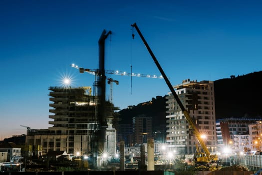 Illuminated construction of multi-storey buildings with tower cranes at sunset. High quality photo