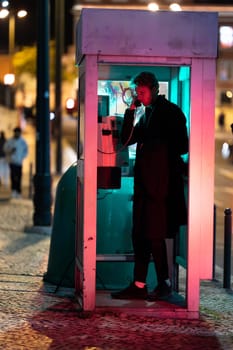 A young man is talking on a phone at noir style in booth The image has a dark and moody atmosphere, with the man's face illuminated by the phone's light