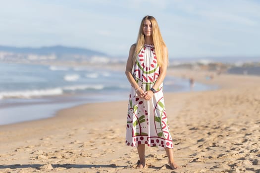 Young woman with long blond hair is posing on the beach with the ocean in the background