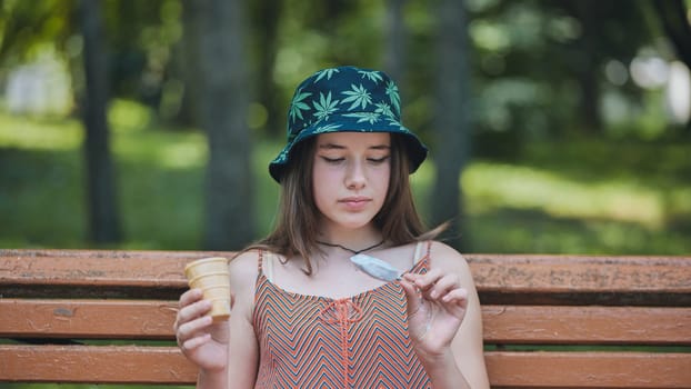 Teenage girl wearing bucket hat with marijuana leaves print enjoying ice cream in park during summer