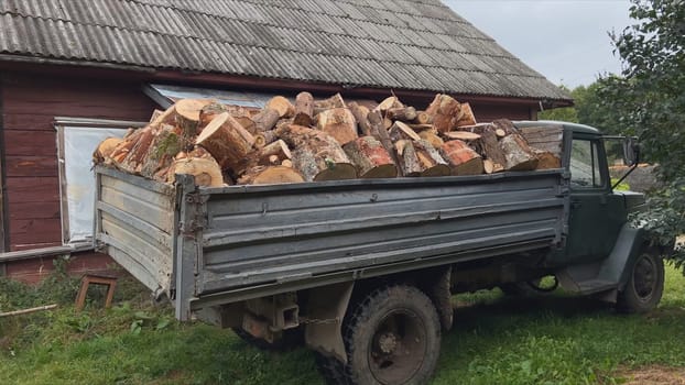 Old truck loaded with firewood parked next to a wooden house in the countryside
