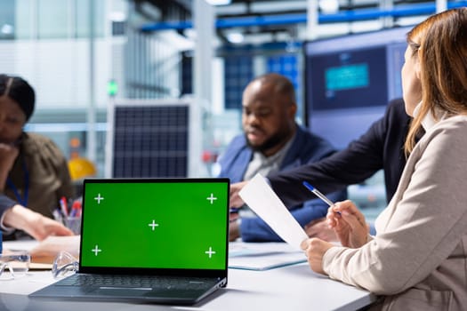 Production plant colleagues look over research and development data on mockup notebook, analyzing innovative manufacturing strategies. Businesspeople brainstorm innovations using green screen laptop