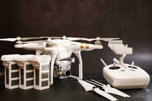 White DJI Phantom 3 drone with spare batteries, propellers and a control panel stands on a black table. High quality photo