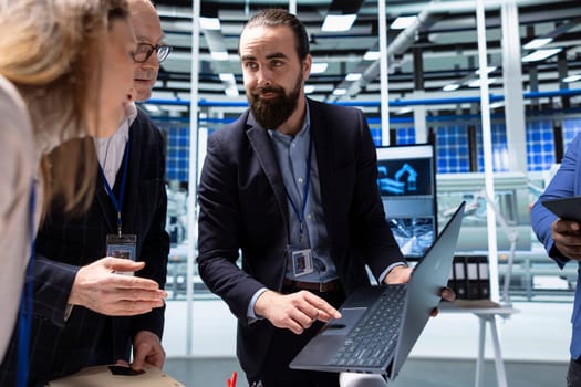 Photovoltaics factory management team looking at manufacturing equipment specifications on laptop. Businesspeople collaborate on green energy strategic investments, looking at data on notebook