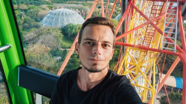Selfie of a happy male tourist traveler in the cabin of a ferris wheel in amusement park on vacation