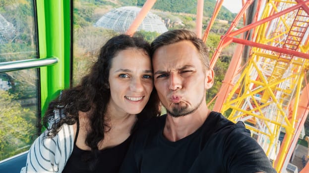 Selfie of happy couple tourists travelers in love in the cabin of a ferris wheel in amusement park on summer vacation