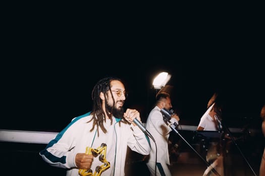 Man with a tambourine sings into a microphone on stage at night near the vocalist and guitarist. High quality photo