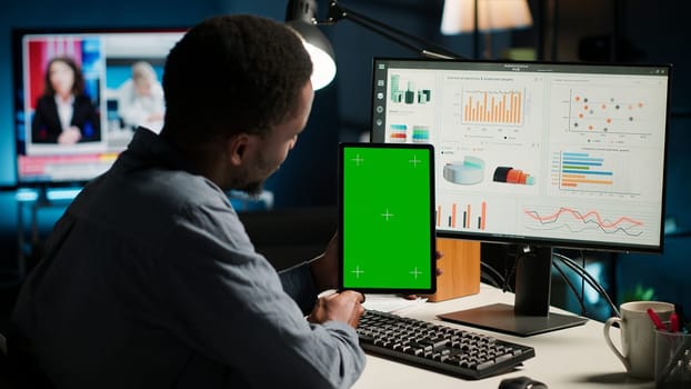 Young guy examining funds for a program and holding tablet with mockup, studying finances and accounting management on a software. Male specialist doing remote work for a startup. Camera B.