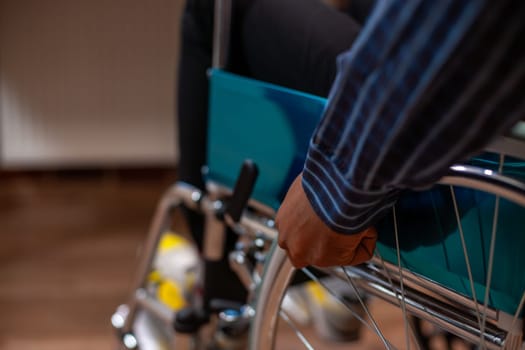 Closeup on hands of african american person spinning wheel of his wheelchair and entering his workplace. Black businessman with disability seated at wheelchair friendly office desk.
