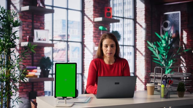 Confident woman solving tasks on a freelance platform next to mockup screen, answering emails and multitasking. Person staying connected and enjoying flexibility of working from home. Camera B.