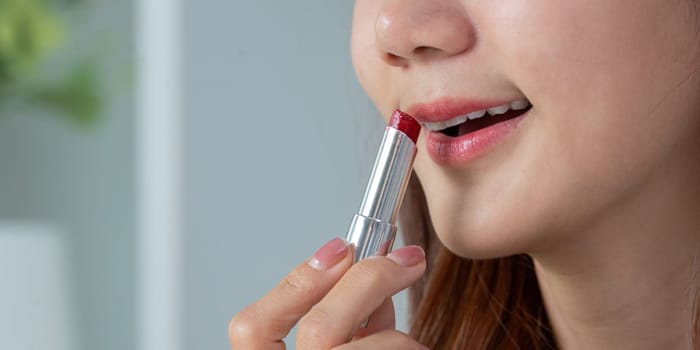 A woman applies vibrant red lipstick, showcasing her beauty routine and the art of makeup application with confidence.