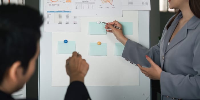 A woman points out critical aspects of her data analysis on a board while her colleague takes notes, illustrating collaborative strategies.