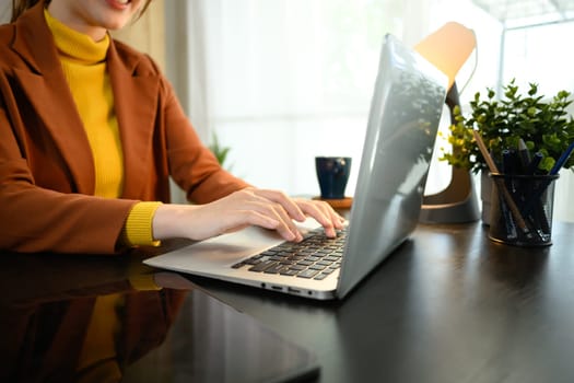 Close up of businesswoman typing on laptop at modern workspace.